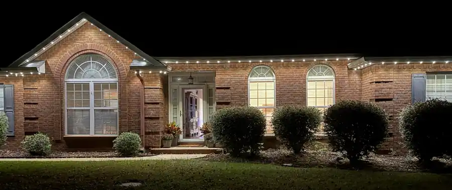 Brick home with permanent roofline lighting glowing warm white at dusk